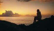 Woman reading a book on rocky beach at sunset in Tenerife.