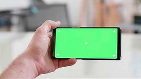 Man hand holding the smartphone horizontally with green screen on. Watching ideos.