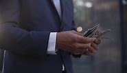 Premium stock video - Unrecognizable businessman on the street holding bundle of american money in his hands, counting it. wealthy male counts hundred