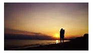 Beautiful couple in silhouette walking and kissing on the beach in...