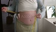 Young woman measuring her pregnant belly with centimeter tape. Preparation for childbirth, Girl big belly advanced healthy pregnancy.