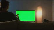 woman is sitting on the couch watching tv with a green screen switching channels with a