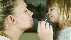 Mother makes up lips with lipstick to the daughter and kisses it, close shot