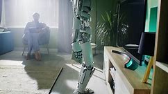 Futuristic android kneeling and removing dust from shelf under TV set while doing household chores near man using tablet at home