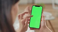 Russia - February 17 2021: Use green screen for copy space closeup. Chroma key mock-up on smartphone in hand. Woman holds mobile phone iPhone and swipes photos or pictures left indoors of cozy home