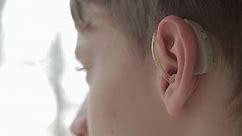 Handsome boy wears a hearing aid. Young man with symptom of hearing loss. Technology helps people with disabilities in their daily lives. Young deaf man adjusting hearing aid to environment.