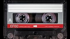 Audio cassette tape in use for sound recording in the tape recorder. A vintage, red and white, brand new blank labelled music cassette playing back in a deck player. Static video camera shot. Close up
