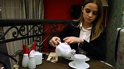 Young girl in jacket and blouse pours tea into a Cup from a teapot to a cafe for dessert