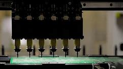 Slow motion: SMT pick and place machine installing SMD electronic components - assembly of printed circuit board: close up front view. Industrial, robotic, production and manufacturing concept