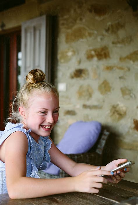 preteen girl laughing while holding her mobile telephone by helen