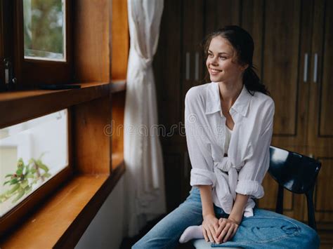 Woman Sitting At Home By A Wooden Window With A Smile On A Chair In