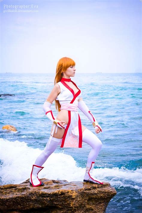 A Woman Dressed In White And Red Standing On Rocks Near The Ocean