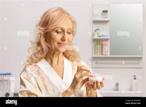 Beautiful Mature Woman In A Bathrobe Holding A Face Cream In A Bathroom