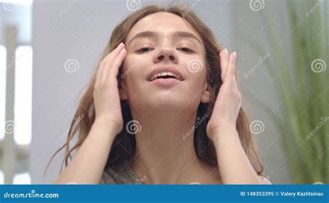 happy woman doing facial massage by hands and looking in bathroom