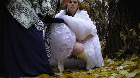 bride struggles with her wedding dress as she pees in the woods