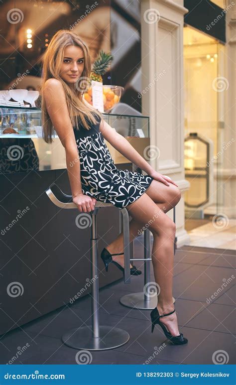 Attractive Blonde Girl With Long Hair Sitting On A High Bar Stool Stock