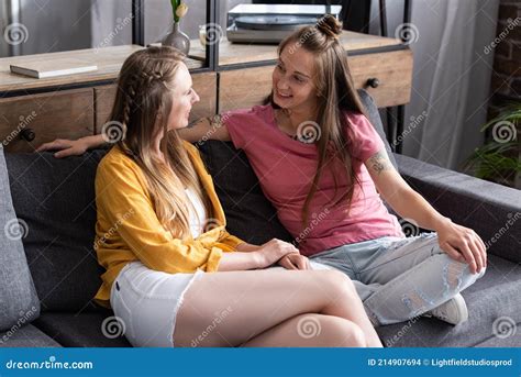 dos lesbianas sonrientes sentadas en el sofá y mirándose en el salón