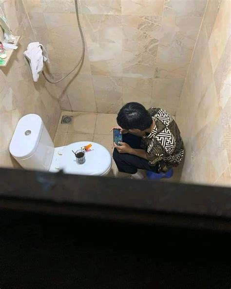 A Man Squatting Down To Take A Photo Of A Toilet In A Bathroom Stall