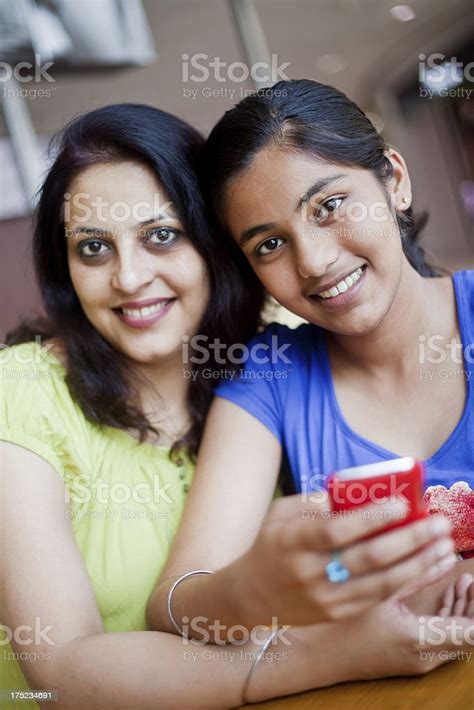 Cheerful Indian Mother And Daughter Sending Reading Sms At Cafeteria