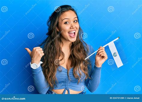 young hispanic girl holding el salvador flag pointing thumb    side smiling happy