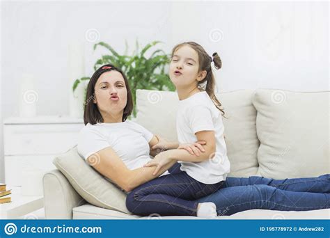 Photo Of Mother And Daughter Sitting On White Sofa And Show Kiss On