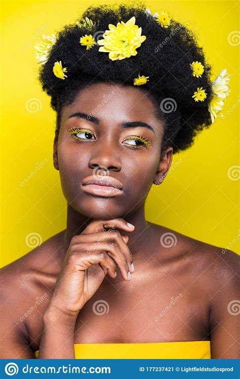 african american girl with flowers in hair looking away on yellow stock