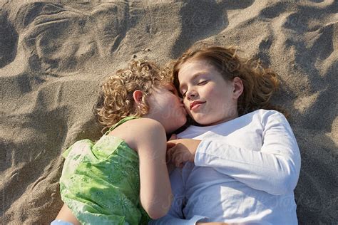 two sisters lying on the beach kissing on the cheek stocksy united