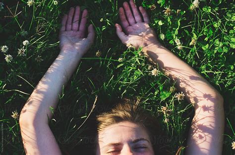 teen lays with arms outstretched in clover covered field by tana teel