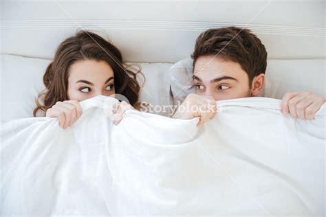 Funny Young Couple Lying And Hiding Under The Blanket In Bed Royalty