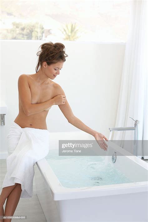 naked woman sitting on edge of bathtub checking water high