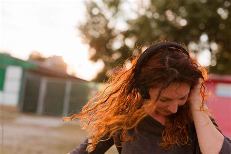 redhead woman listening music outdoors del colaborador de stocksy