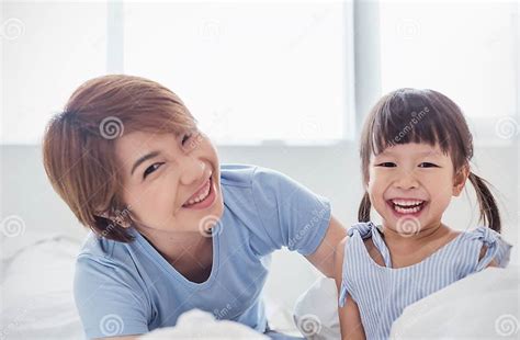 asian mom and her little daughter are cuddling and smiling in white bed