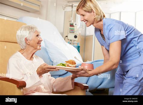 Nurse Serving Meal To Senior Female Patient Sitting In Chair Stock