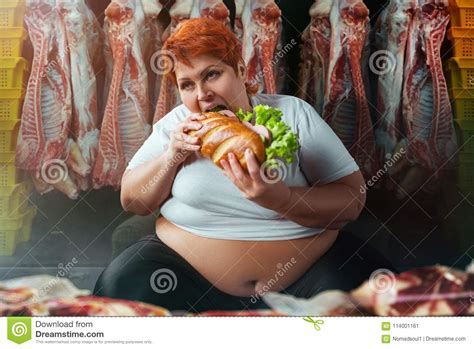 Fat Woman Eating Burger Against Meat Carcasses Stock Image