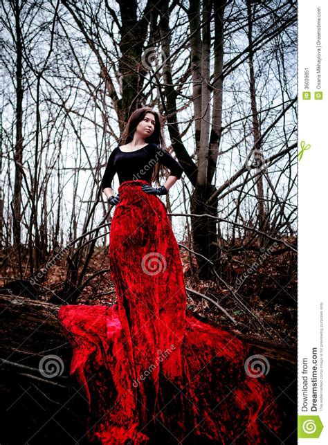 Mysterious Woman Or Witch In Long Red Dress Standing In Dark Forest