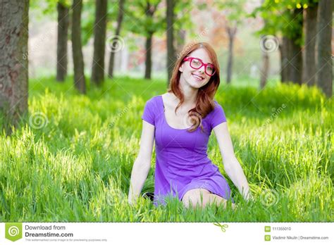 Redhead Girl In Eyeglasses Sitting On Green Grass Stock