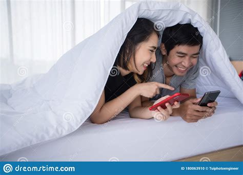 Asian Couple Lovers Lying On Their Play Mobile Phones On Bed At Home