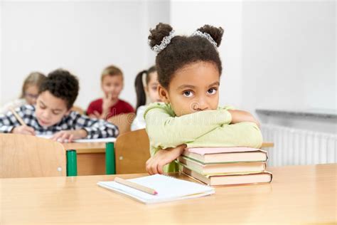 Schoolgirl Sitting At Desk In Classroom Leaning On Books Stock Image
