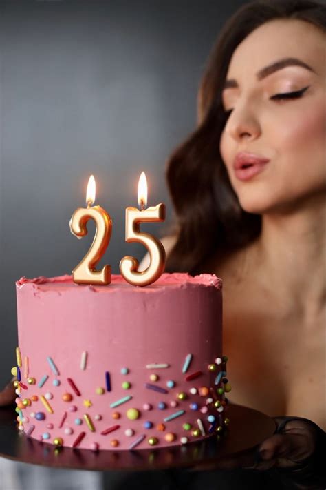 a woman blowing out the candles on her pink birthday cake with sprinkles