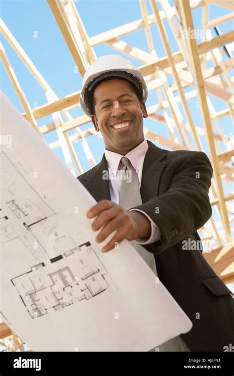 smiling surveyor  hard hat  building plans  construction site  angle view stock
