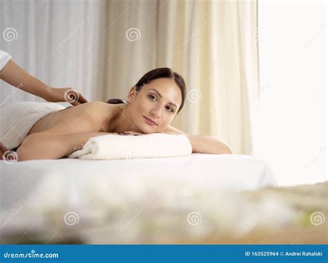 pretty brunette woman enjoying treatment with hot stones in spa salon
