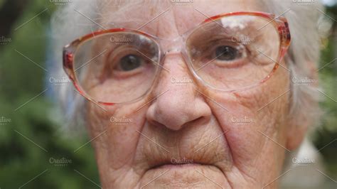 old woman in glasses looking into camera outdoor portrait of sad