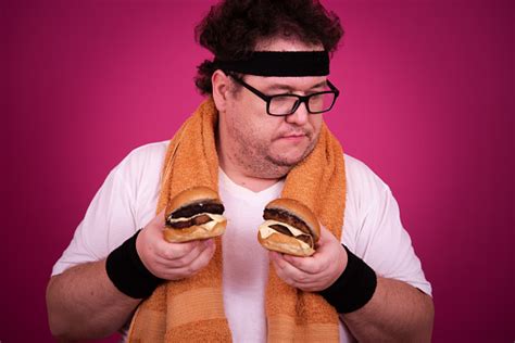 Funny Fat Man Is Engaged In Fitness And And Greedily Eats A Hamburger