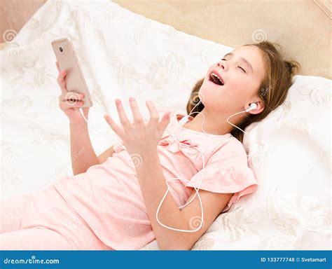 leuk meisje die op het bed liggen die aan muziek en het zingen luisteren stock foto image