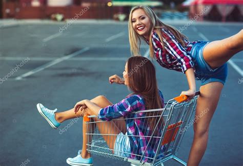 two happy beautiful teen girls driving shopping cart