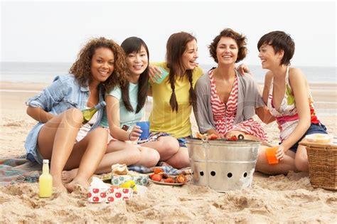 group of girls enjoying barbeque on beach together stock