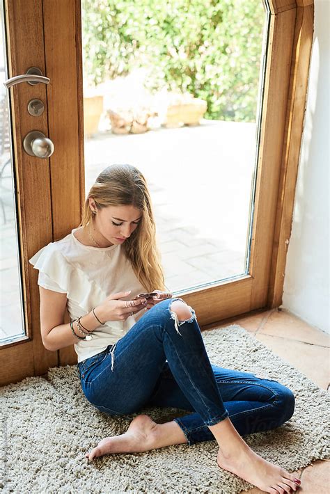 Barefoot Woman In Ripped Jeans Browsing Cell Phone On Rug
