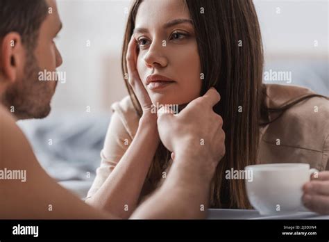 Blurred Man Touching Face Of Brunette Girlfriend With Cup Of Coffee In