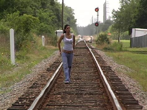 a beautiful latina brunette walks toward the camera down a lonely stretch of railroad track