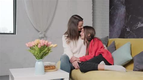 Mother Hug And Kiss Her Daughter While They Are Sitting On Sofa And